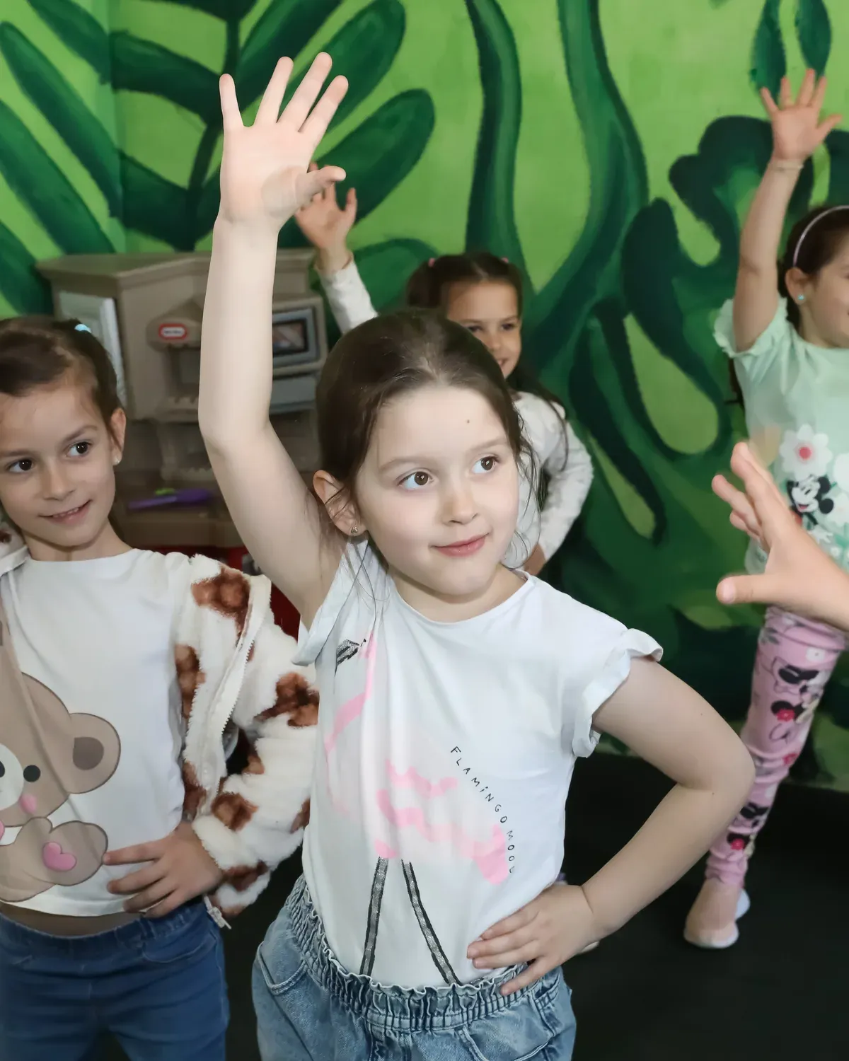 Copii dansând cu mâinile ridicate, în fața peretelui pictat cu junglă