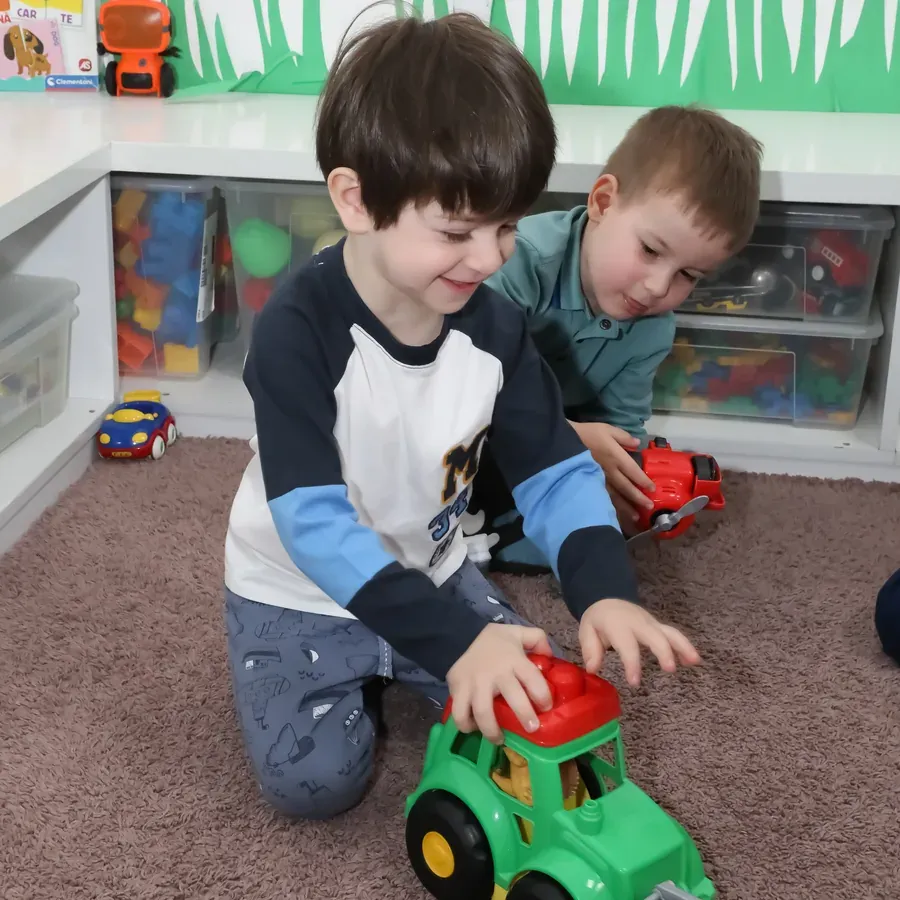 Doi băieți jucându-se cu un tractor, pe covorul din sală