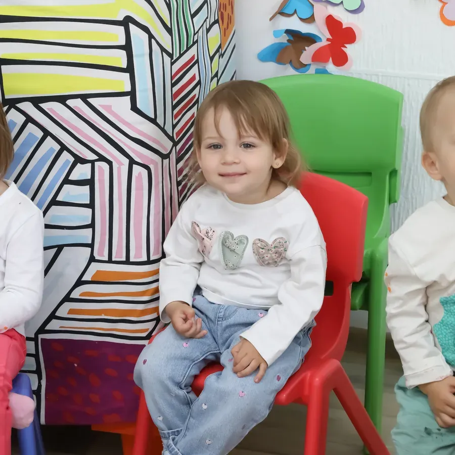 Copil de creșă, zâmbind pe un scăunel din sala de grupă