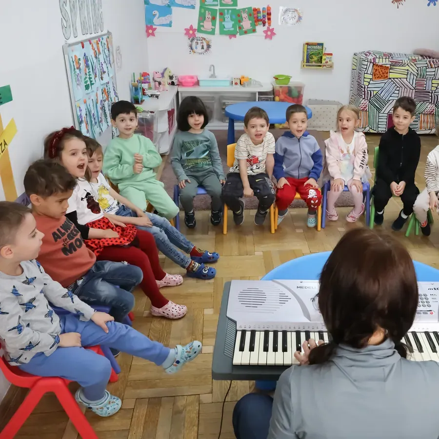 Ora de muzică: grupa așezată în semicerc, în jurul pianului